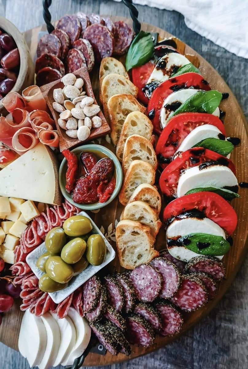 Runde Holzplatte mit Caprese aus Tomate und Mozzarella, dazu Salami, Prosciutto, Weißbrot und Oliven