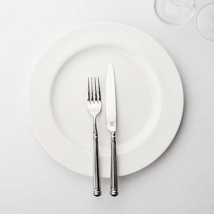 Weißer Porzellanteller mit Messer und Gabel, im Hintergrund zwei Gläser