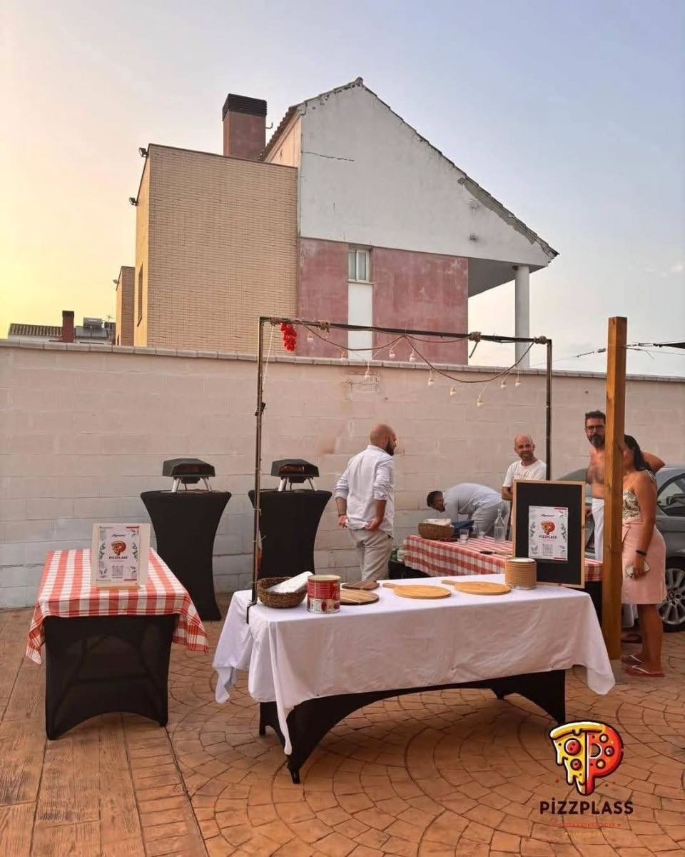 Zwei mobile Pizza-Öfen auf Stehtischen bei einer Feier im Freien, dazu Lichterkette und eingedeckte Tische