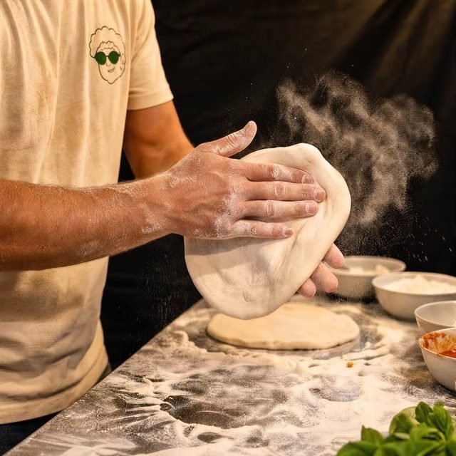 Bemehlte Hände drücken einen Teigling flach, eine Mehlwolke stiebt zur Seite