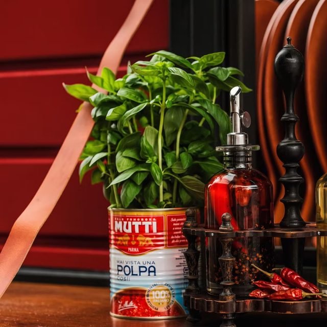 Basilikumtopf in einer Tomatendose, daneben ein Ständer mit Öl- und Chiliflaschen auf einem Holztresen