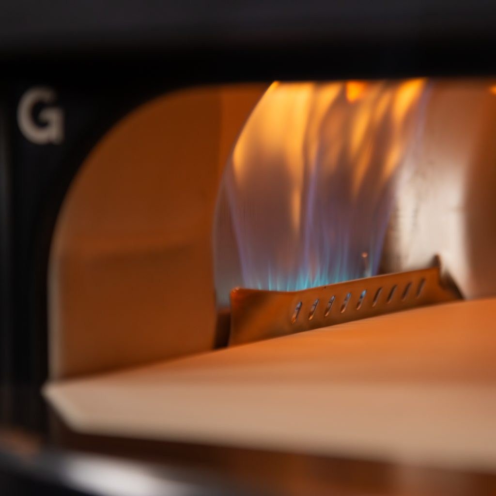 Nahaufnahme einer orange-blauen Flamme im Gozney-Ofen über dem Backstein.